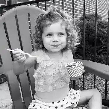 a child sitting in a chair holding a spoon and a cup of yogurt